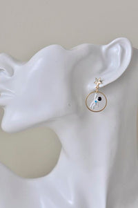 White astronaut charm inside gold hoop earring with gold star stud, shown worn on ear