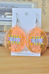 Pair of orange glitter perspex Tamagotchi drop earrings on Kaboodle Designs card