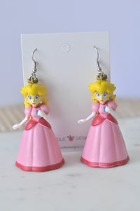 Two Princess Peach plastic figure earrings on a Kaboodle Designs card, pink dress and crown visible