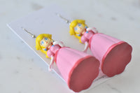 Close-up angled view of Princess Peach earrings showing dress hem and painted face detail