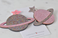 Close-up of two glitter Saturn earrings showing ring detail and mixed pink and multicolour glitter finish