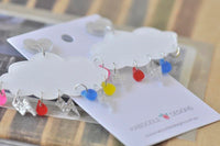 Pair of cloud earrings on backing card showing glitter heart studs and rainbow drop charms