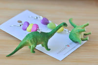 Brontosaurus earrings on card next to toy dinosaur figures, showing full heart bead strand