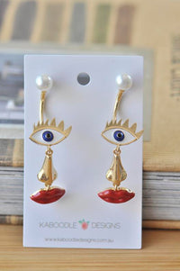 Gold face-shaped drop earrings with eye, nose and red lips on Kaboodle Designs card