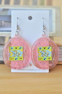 Pink glitter Perspex Tamagotchi drop earrings on card, showing pixel screen detail