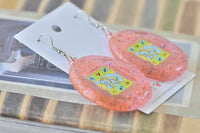 Pair of pink Tamagotchi drop earrings lying on earring card, front view