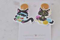 Close-up of black kitten earrings with mustard yellow stud tops and colourful printed detail