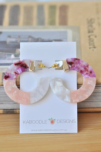 Round acrylic hoop earrings in purple, pink and white marbled tones displayed on a card