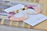 Pair of purple, pink and white acrylic hoop earrings laid flat with gold hardware visible