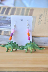 Green stegosaurus dangle earrings with pink, purple and orange heart beads on jewellery card