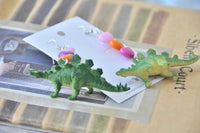 Two stegosaurus dinosaur figures with heart bead earrings resting on jewellery card