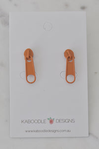 Pair of orange zip-pull stud earrings on a Kaboodle Designs earring card