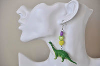 Close-up of green brontosaurus earring with purple, green and yellow heart beads worn on a model's ear