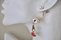 Close-up of earring detail showing enamel eye, gold nose charm and red lip charm
