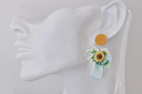Close-up side view of sunflower and hydrangea jar earring worn on a display ear