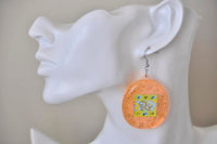 Close-up of orange Tamagotchi earring worn on ear against white mannequin bust