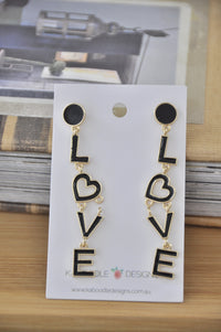 Black enamel LOVE letter drop earrings on card with gold outlines, front view of pair