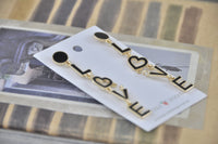 Close-up of LOVE earrings laid flat showing gold trim and black enamel finish on each letter