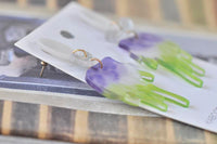 Close-up of paired brush earrings on card showing glitter bow detail and jump rings