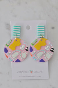 Round resin drop earrings with pink geometric pattern and mint striped stud, on card