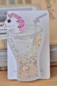 Acrylic unicorn brooch shaped like a glittery milkshake glass with pink-maned unicorn head, on card backing