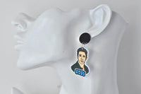 Close-up of Ross earring on ear showing black stud and illustrated portrait charm