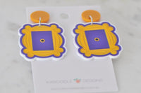 Pair of yellow and purple peephole frame earrings laid flat against backing card, front view