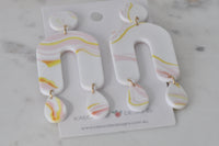 Pair of marbled arch drop earrings laid flat on marble surface, showing full length