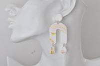 Close-up of marbled arch earring worn on ear, showing pink and yellow swirl detail