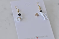 Pair of astronaut drop earrings laid flat showing spaceman and star charms