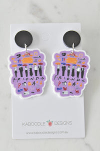 Purple acrylic Friends TV show collage drop earrings on black stud backs, flat lay on Kaboodle card