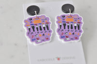 Pair of Friends collage drop earrings hanging from black round studs against marble background