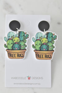Pair of acrylic Free Hugs cactus drop earrings on black round studs, front view