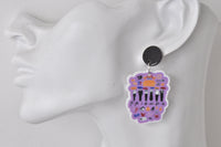 Close-up of single Friends collage earring worn on ear, showing character silhouettes and logo