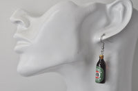 Close-up of a single VB bottle earring worn on an ear, showing glossy resin finish