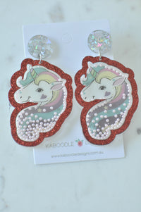 Front view of unicorn shaker drop earrings with red glitter edge and pearl beads on Kaboodle card