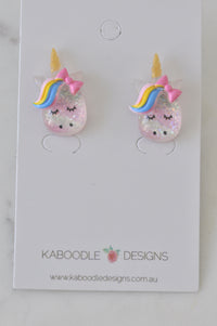 Pair of glitter unicorn stud earrings with rainbow mane and pink bow on card