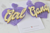 Close-up angled view of Girl Gang earrings showing glitter texture and mirror-gold lettering