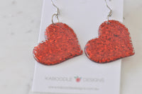 Close-up of two red glitter heart earrings showing glossy perspex finish