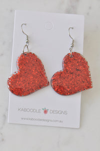 Pair of red glitter heart drop earrings on a Kaboodle Designs card, front view