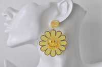 Close-up of sunflower earring worn on ear showing smiley face and star glitter detail
