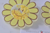 Macro shot of acrylic sunflower earring showing star-filled shaker smiley centre and petal outline