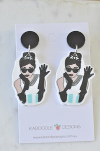 Pair of acrylic drop earrings on card, featuring a black-and-white illustrated woman in sunglasses, pearls and gloves with a