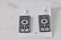 Black and white The Sun tarot card earrings laid flat on marble background