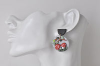 Close-up of clay mushroom earring worn on ear, showing red spotted toadstool cap and black top