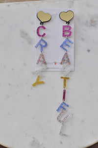Pair of glitter letter drop earrings spelling CRAZY and BEAUTIFUL on gold heart studs on white card