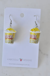 Pair of resin popcorn tub earrings with yellow popcorn label on white card