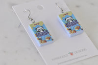 Close-up angled view of Hello Panda earrings showing glossy resin finish and packaging detail