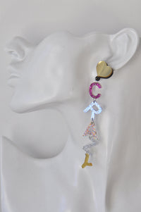 Close-up of CRAZY letter earring on ear-shaped display, showing pink, blue and silver glitter letters