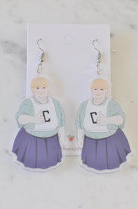 Pair of acrylic drop earrings depicting Sharon from Kath and Kim in netball bib and purple skirt, front view on card